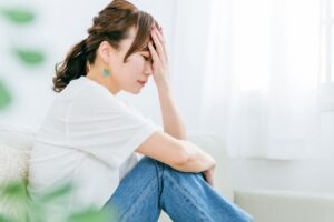 膝に右腕を置いて座り左手を額に当てる女性